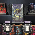 Curio Clip-On Posable Gothic Demon Bat Wings attached to a Curio Candy Floating Book Display Hanger, showing open and closed posable positions with Sarah J. Maas's House of Sky and Breath on a dark romance bookshelf.