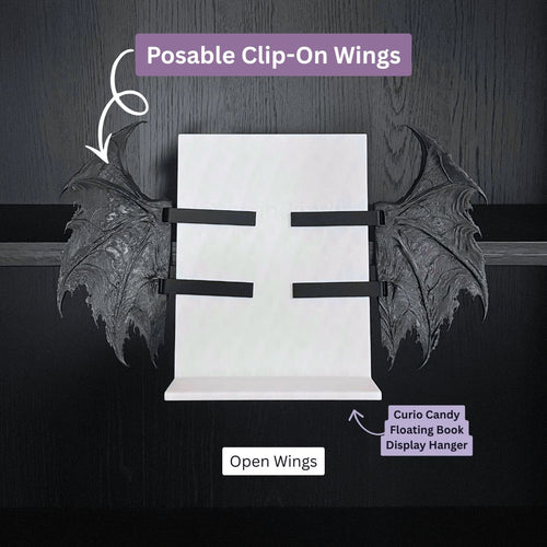 Curio Posable Clip-On Gothic Demon Bat Wings shown in the open position attached to a Curio Candy Floating Book Display Hanger mounted on a bookshelf.
